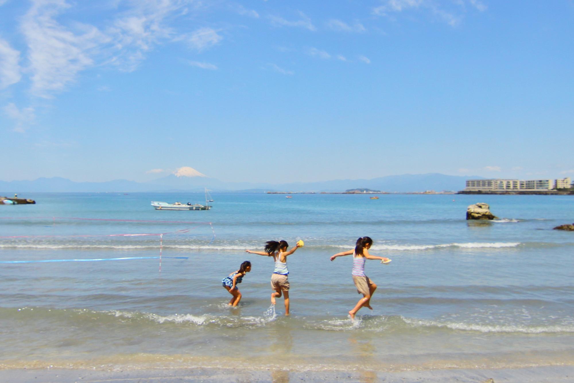 富士山を望む海辺で波打ち際を走る子どもたち